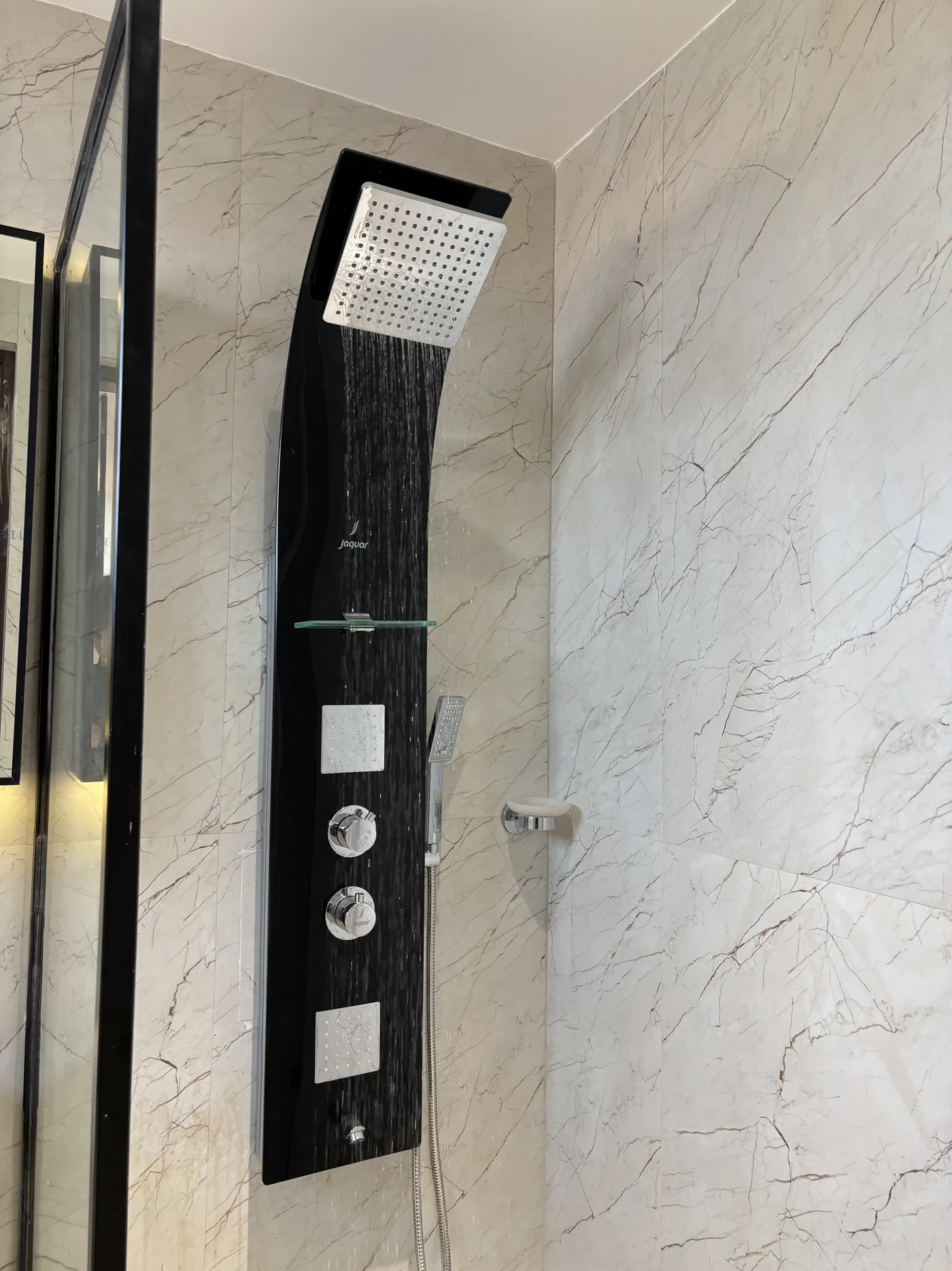 Black shower panel with body jets against a marble-tiled wall