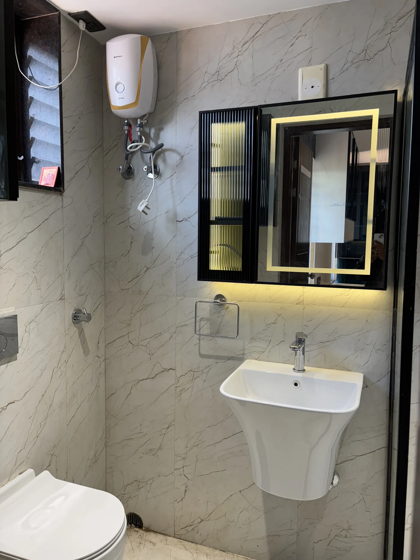 Bathroom with a pedestal basin, backlit mirror and marble tiling