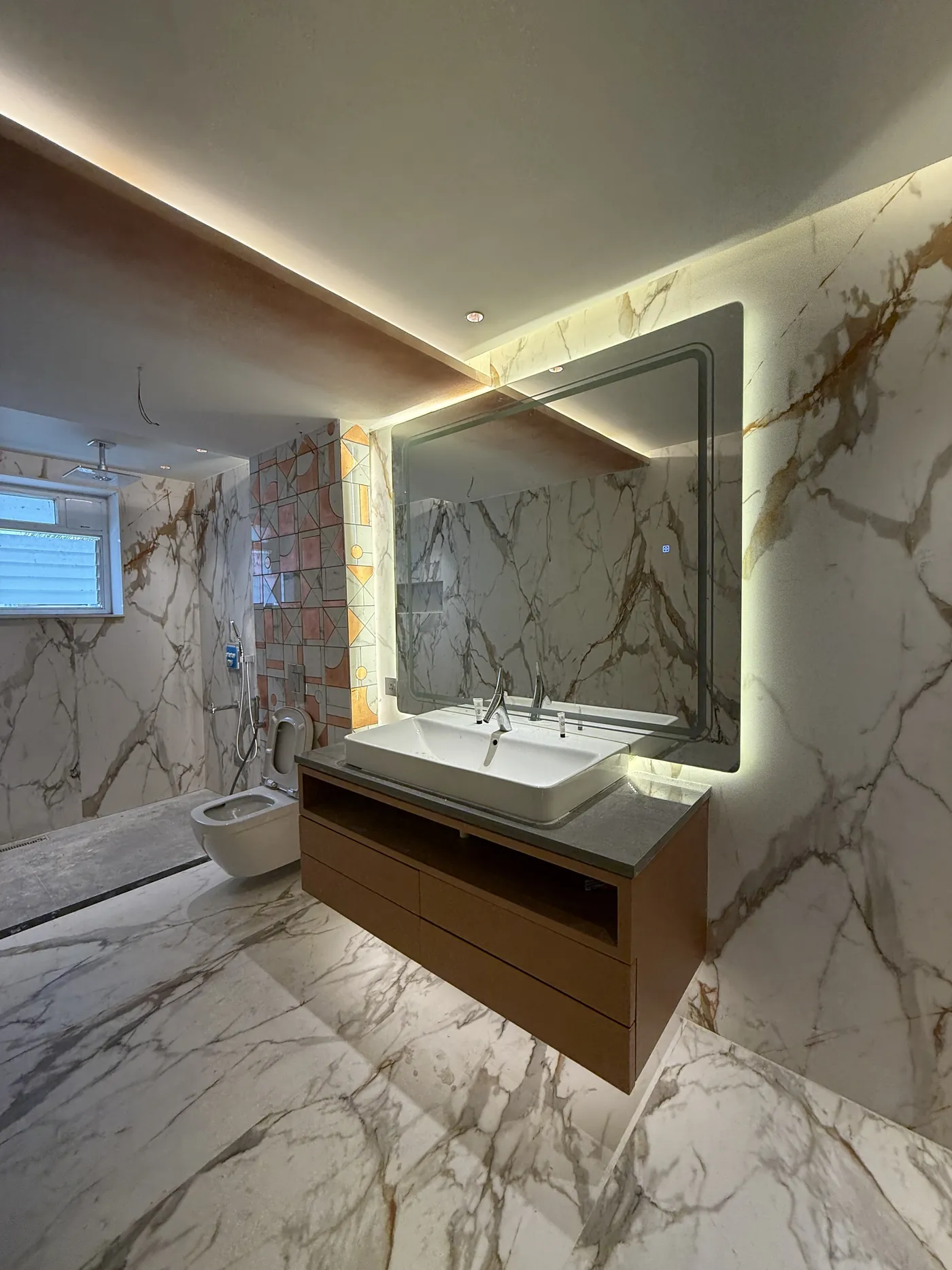 Bathroom vanity with a backlit mirror against book-matched marble