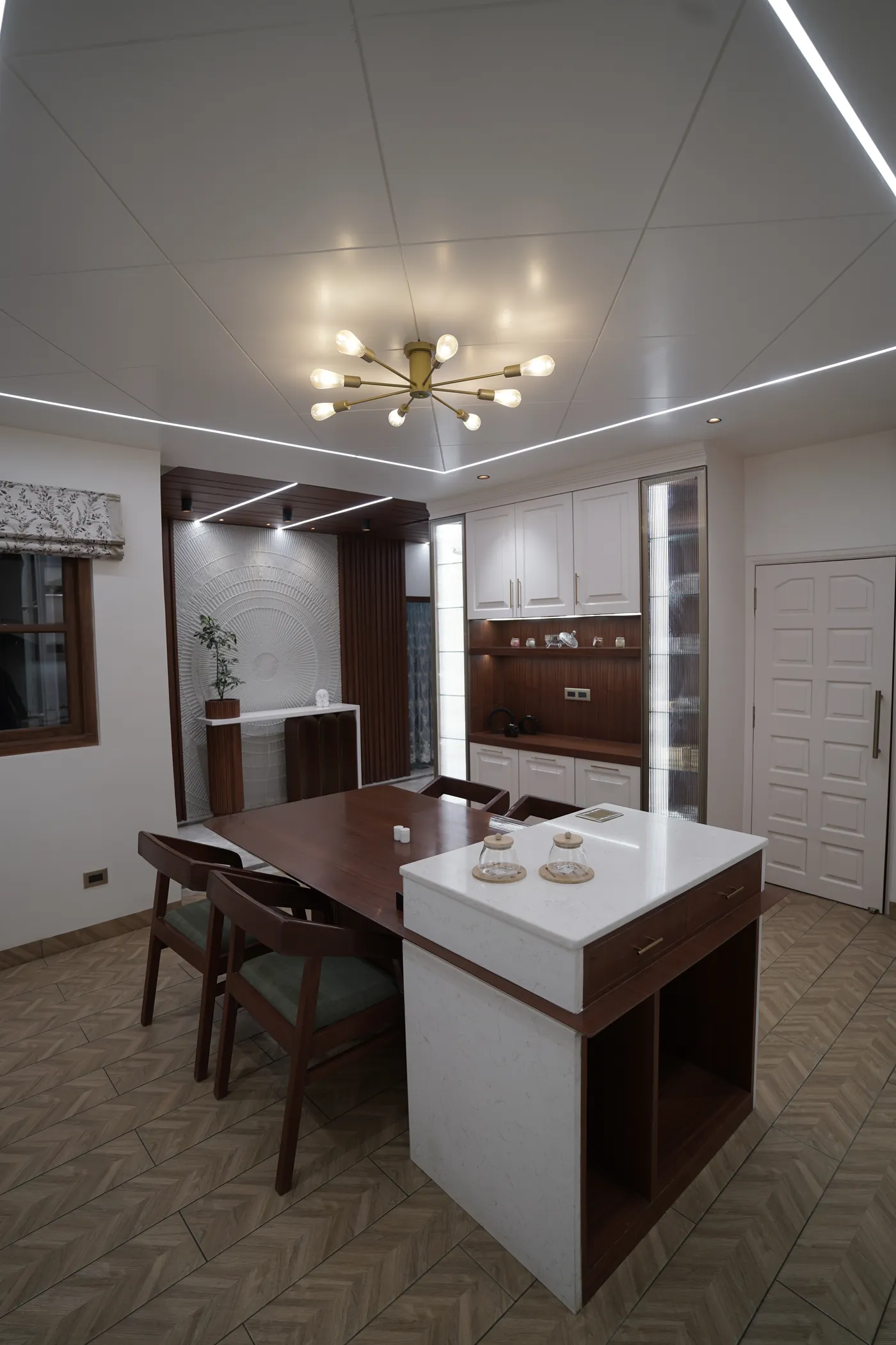 Dining table beside a kitchen island under a linear cove-lit ceiling