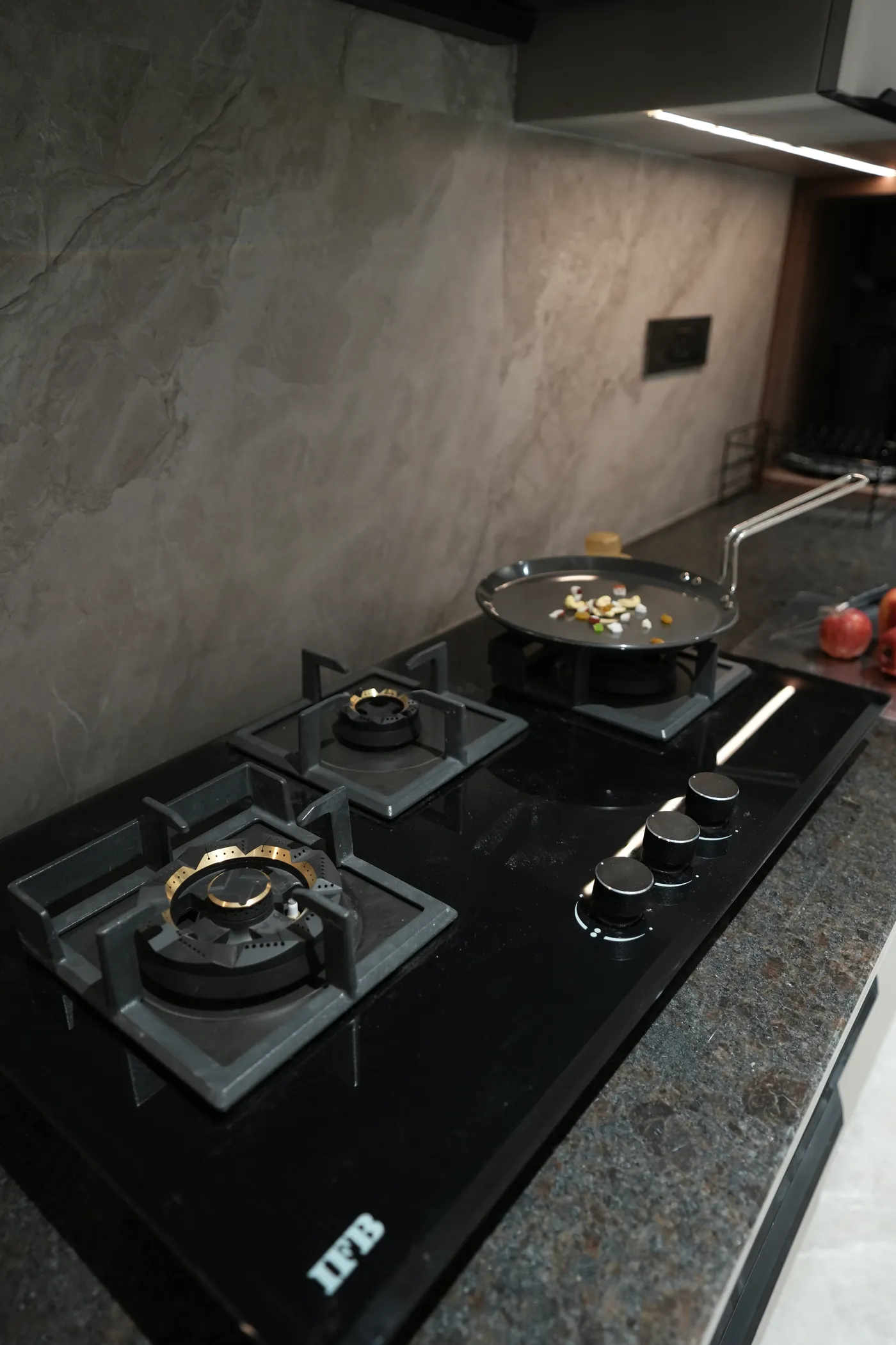 Close view of a gas hob on a dark stone worktop with a marble splashback
