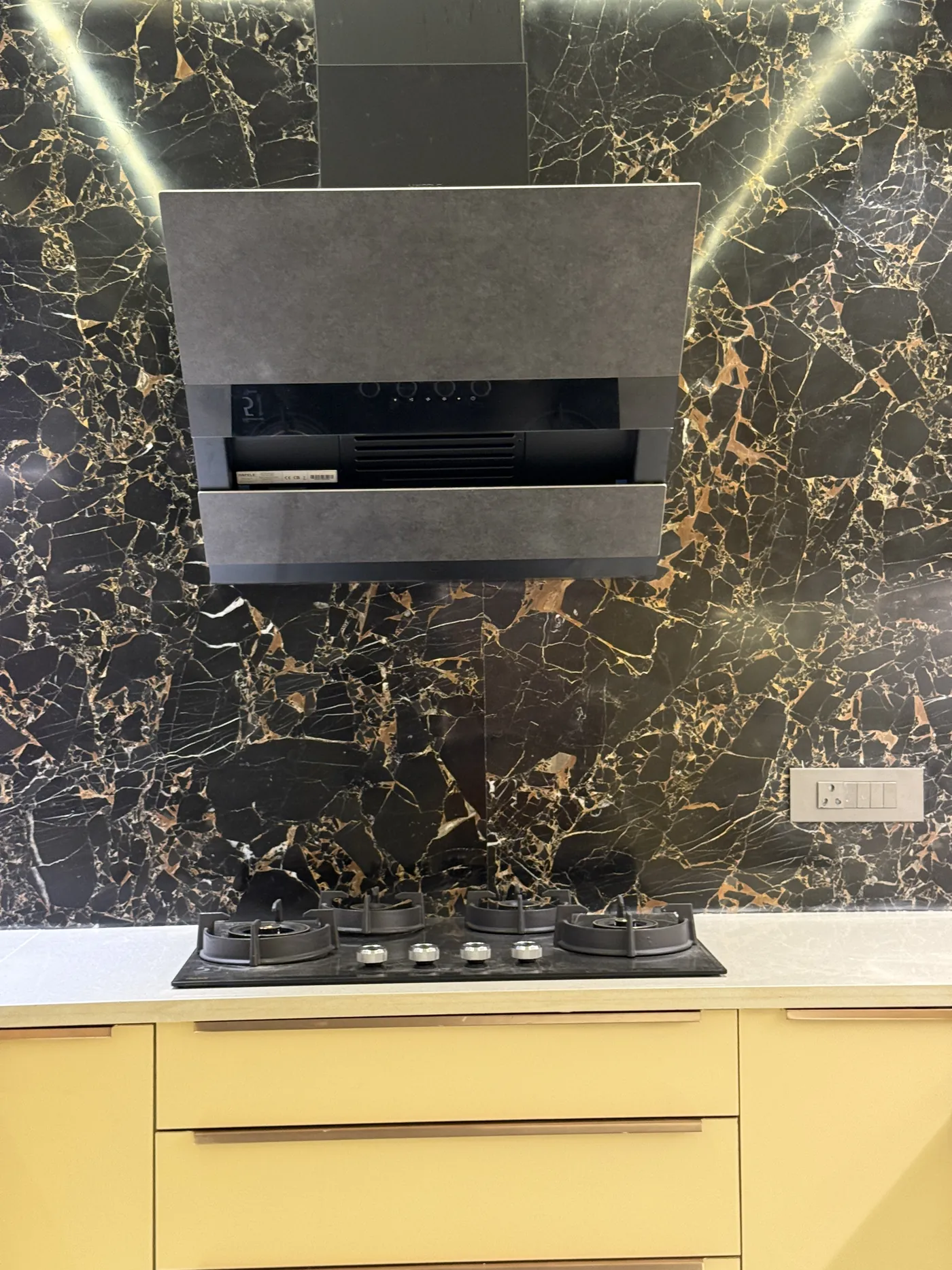 Hob and chimney against a black marble splashback with cream units